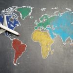 Guided Tours - Top view of crop anonymous person holding toy airplane on colorful world map drawn on chalkboard