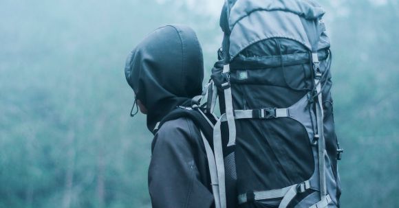 Adventure And Safety - Man Wearing Black Hoodie Carries Black and Gray Backpacker Near Trees during Foggy Weather