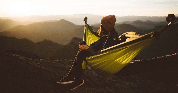 Hiking Times - Unrecognizable woman sitting in hammock above mountains